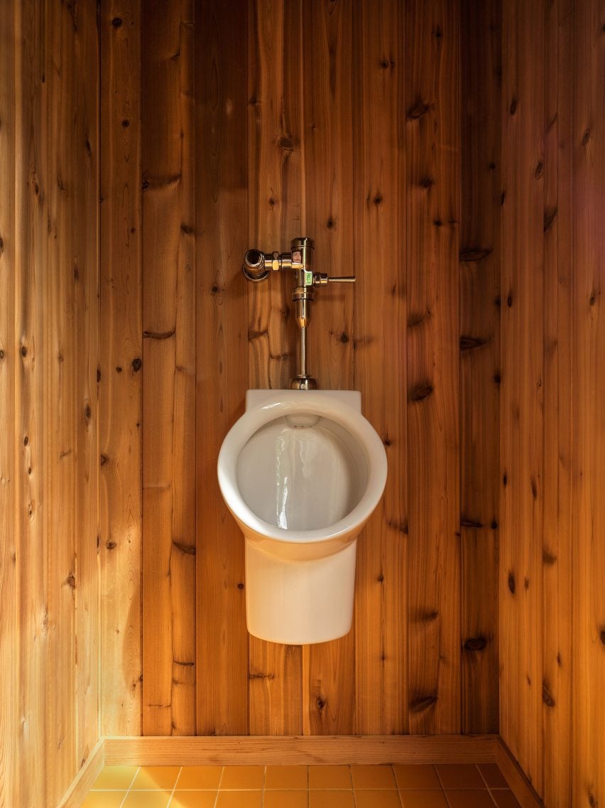 Wall-mounted urinal within a wood-lined space